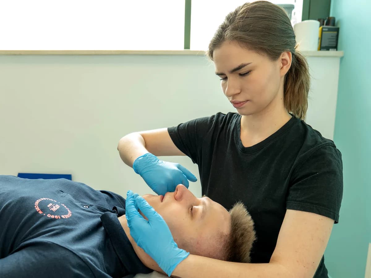 Terapia stawu skroniowo-żuchwowego — fizjoterapeutka w rękawiczkach pracuje przy żuchwie pacjenta