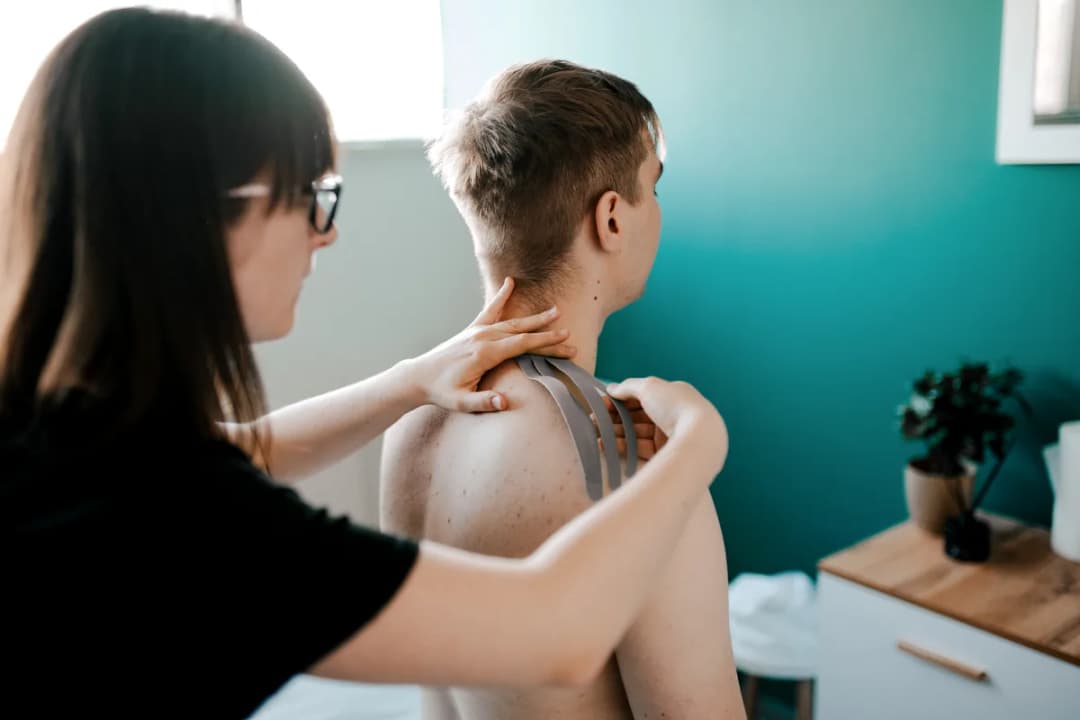 Kinesiotaping w M&M Zdrowy Masaż — fizjoterapeutka aplikuje taśmy na kark i bark pacjenta w gabinecie z turkusową ścianą