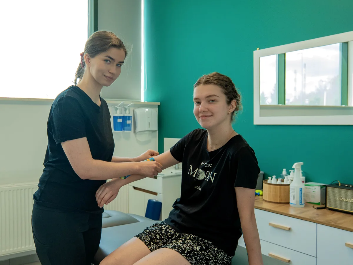 Kinesiotaping w M&M Zdrowy Masaż — fizjoterapeutka aplikuje taśmę na ramieniu siedzącej pacjentki