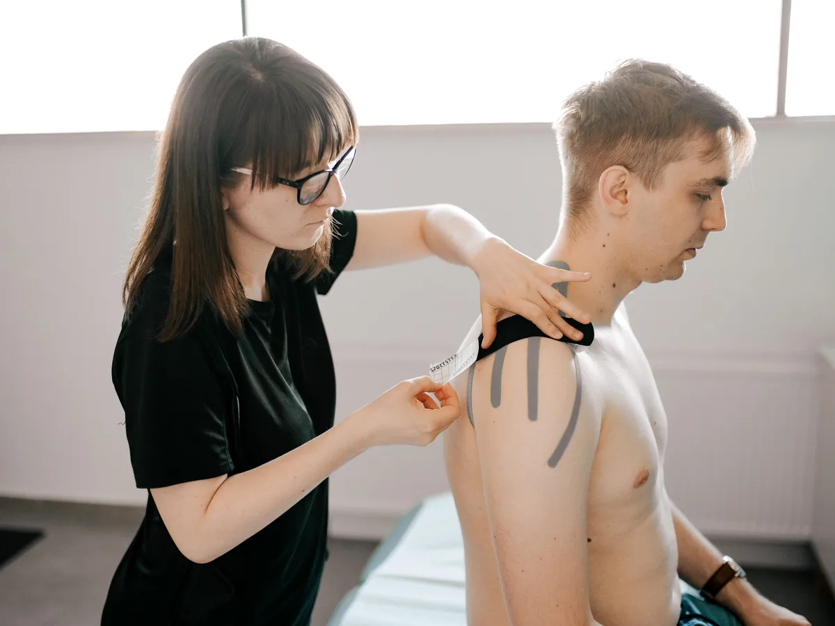 Kinesiotaping karku i obręczy barkowej — czarna taśma aplikowana na plecy pacjenta w gabinecie M&M