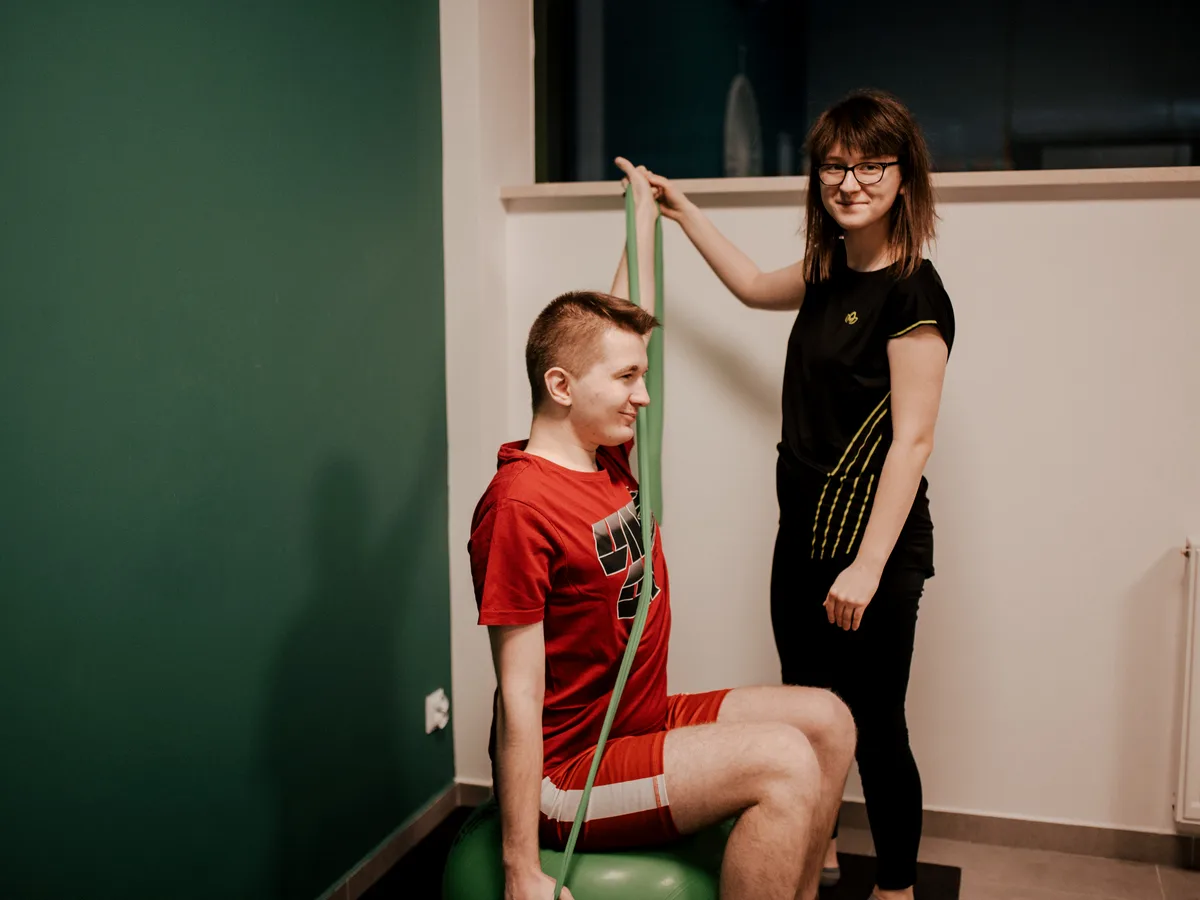 Ćwiczenia z taśmą oporową w gabinecie M&M Zdrowy Masaż — fizjoterapeutka prowadzi pacjenta przez ruch